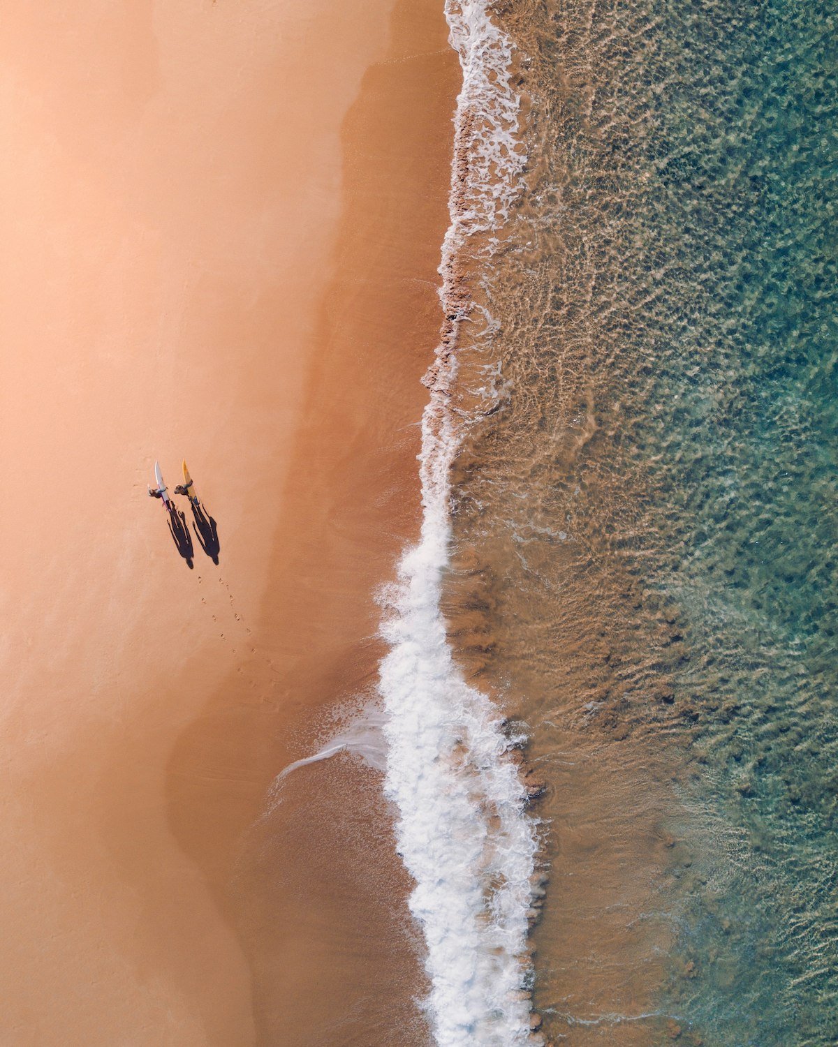 Aerial view of the beach with two people walking along the sand